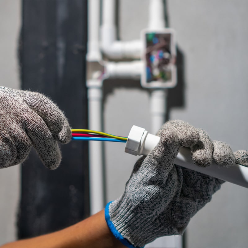 Electrician with gloves installing electrical wiring in PVC conduit.