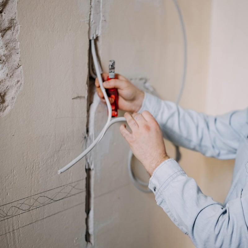 Person repairing wall socket, wiring cables with tool. Home electrical maintenance.