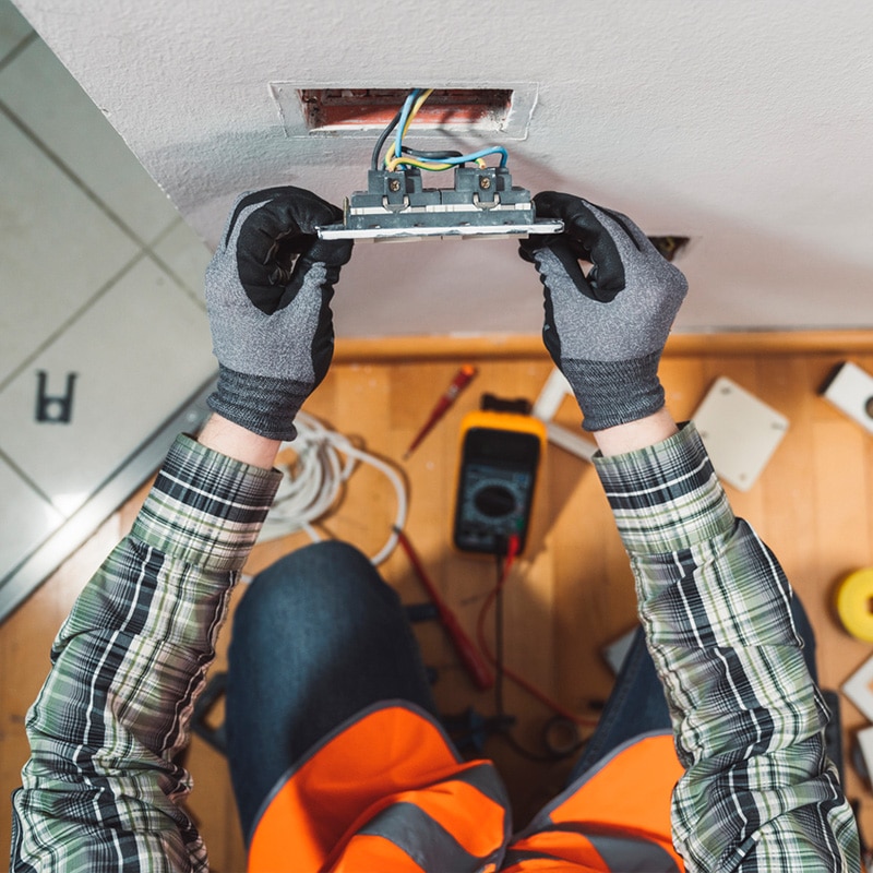 Electrician installing a wall socket with tools and safety gear.