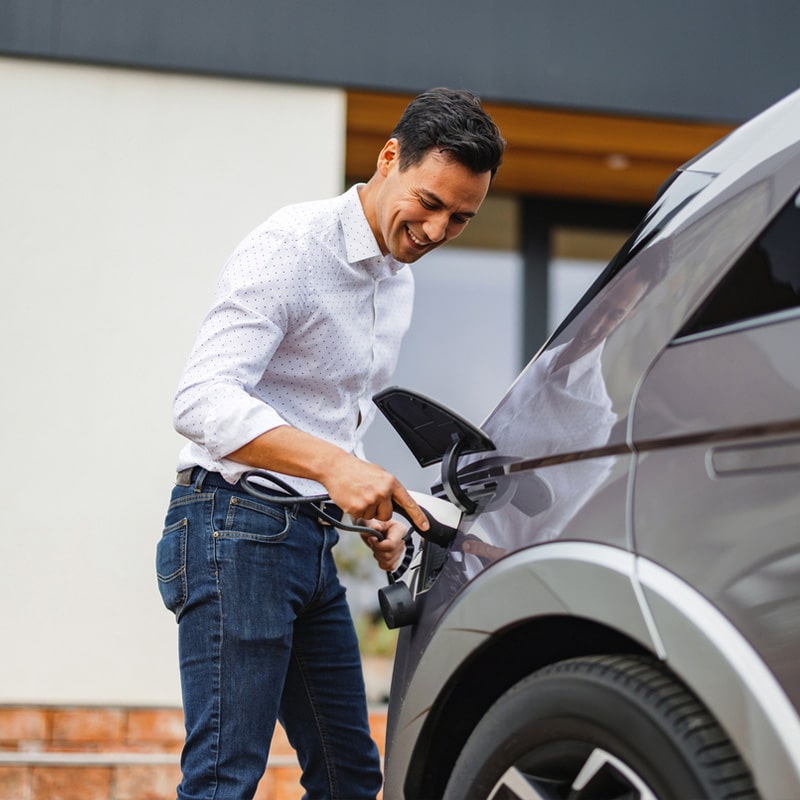 Man charging electric car at home, smiling while plugging in the charger for eco-friendly transportation.