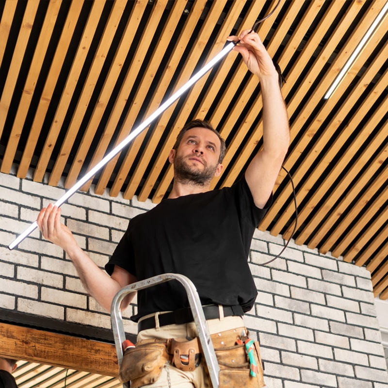 Man installing LED light tube on ceiling while standing on ladder.