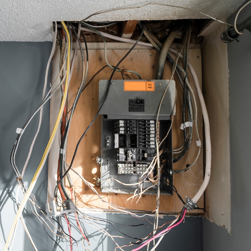 Electrical panel with exposed wires and circuitry, highlighting repair needs in a residential setting.