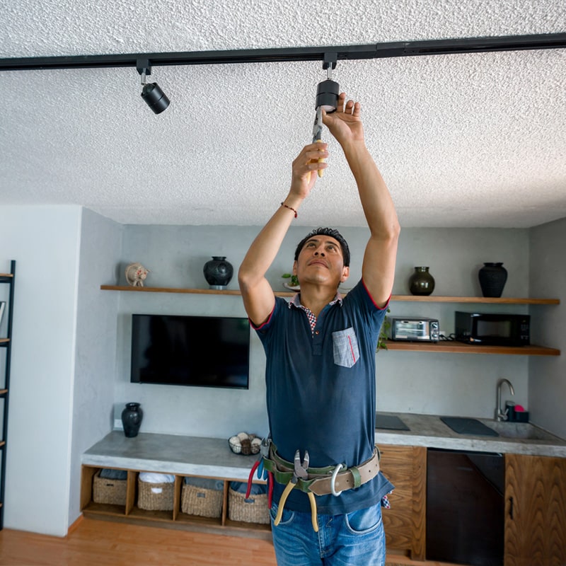Electrician installing ceiling track lighting in modern living room.