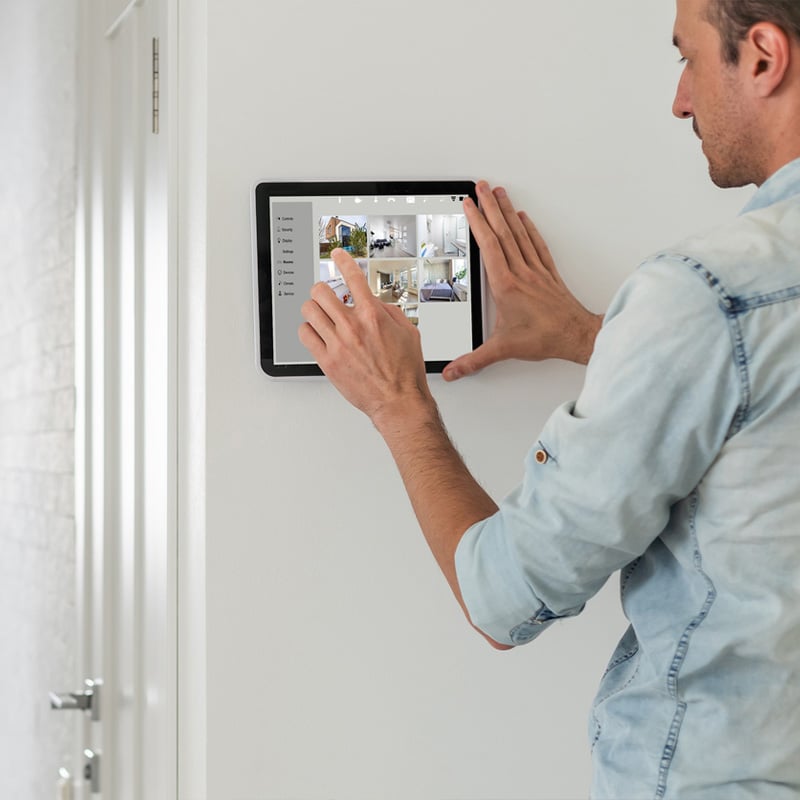 Man interacting with smart home tablet control on wall for security and device management.