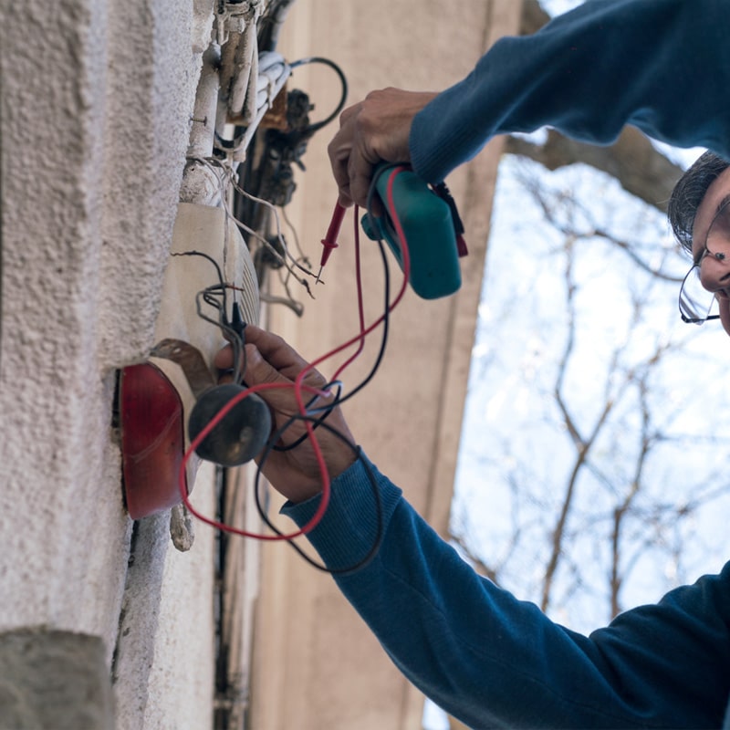 Electrician repairing outdoor wiring with a multimeter on a sunny day.