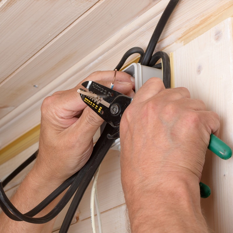 Electrician using wire stripper for safe electrical installation in wooden wall.