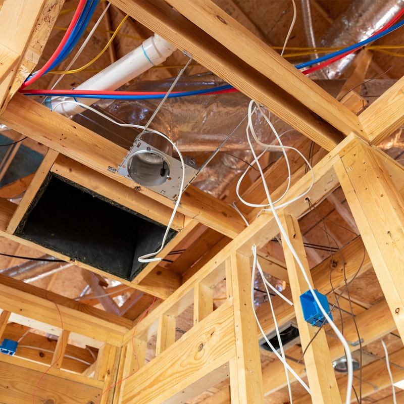 Wooden ceiling framing with electrical wiring and ductwork exposed during home construction.