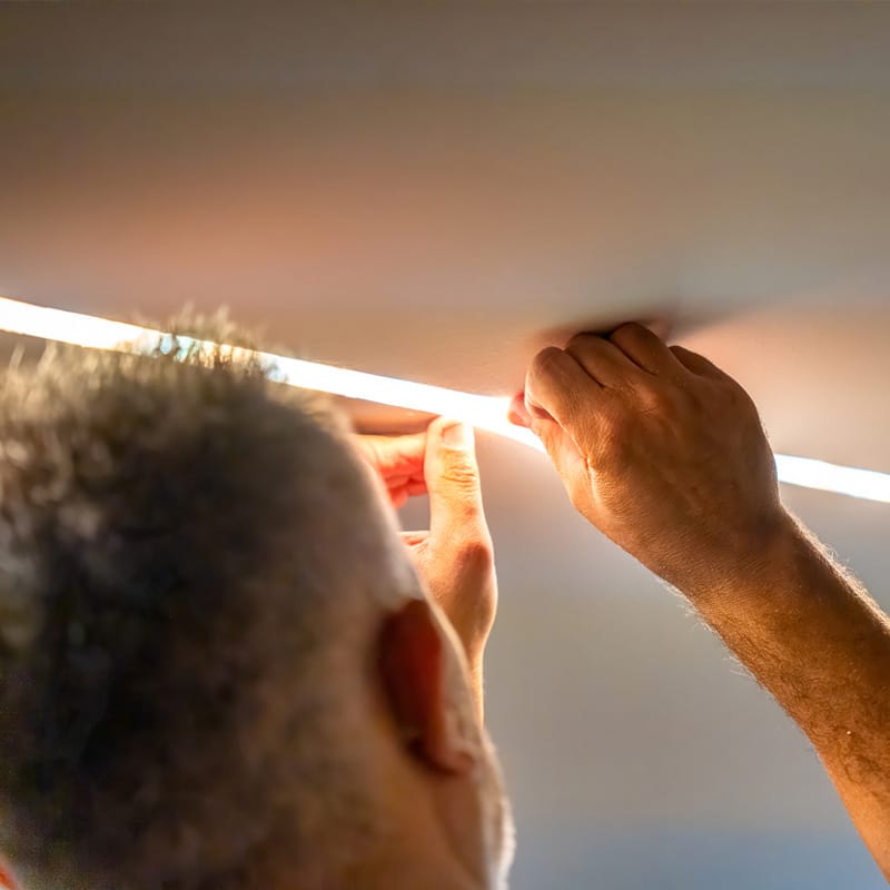 Installing LED strip lights on ceiling for modern ambient lighting.