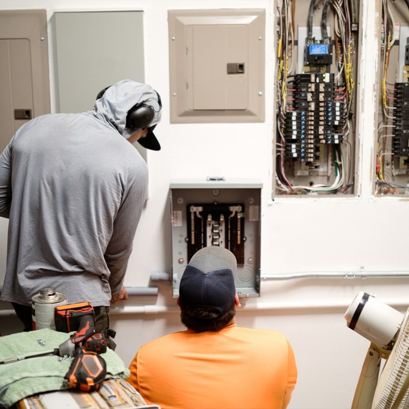 Two electricians inspecting and working on a circuit breaker panel for maintenance and repairs.