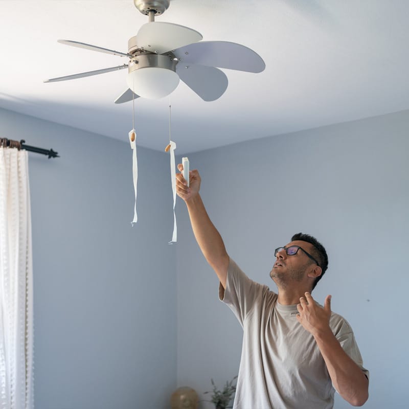 Man adjusting ceiling fan speed in a room, looking up at the blades.