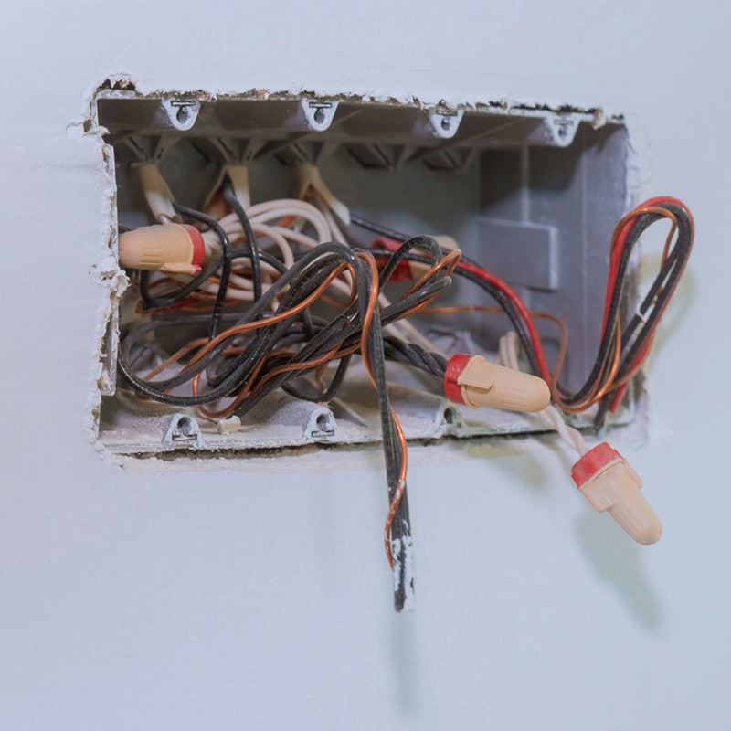 Exposed electrical wiring in a wall junction box with wire connectors for home repair or electrical work.