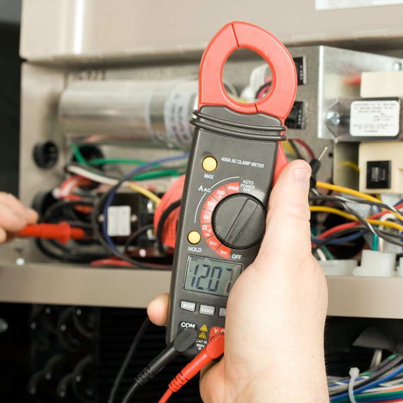 Electrician using a digital clamp meter to measure voltage in a control panel.