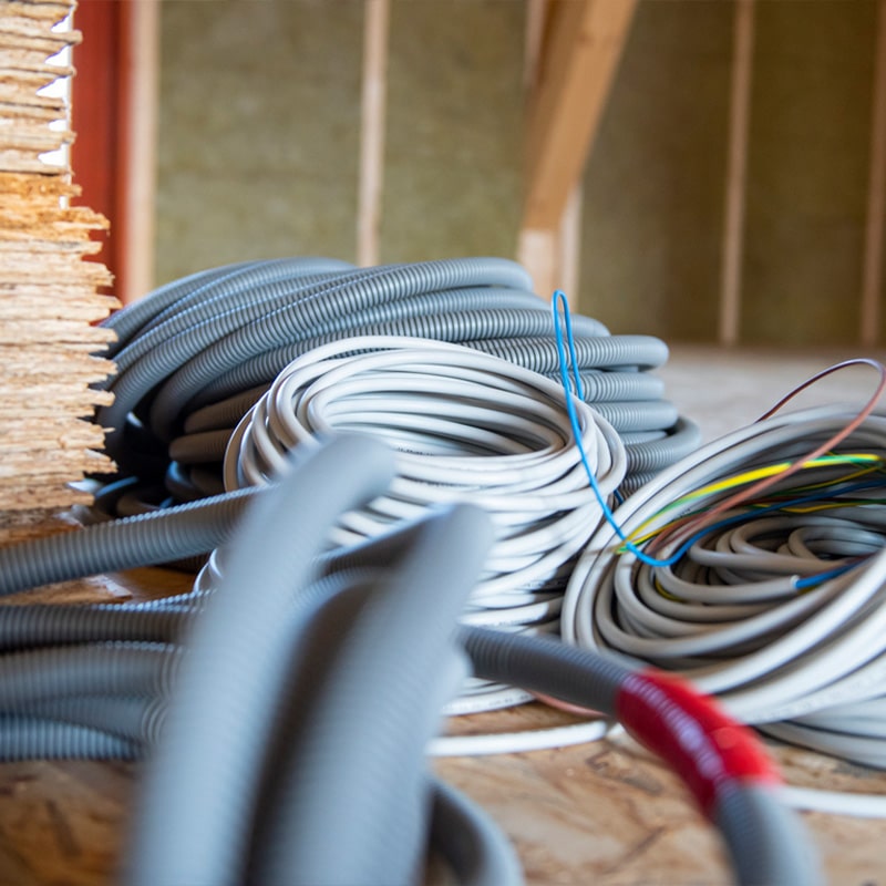 Coiled electrical wires and cables on wooden floor during house construction.