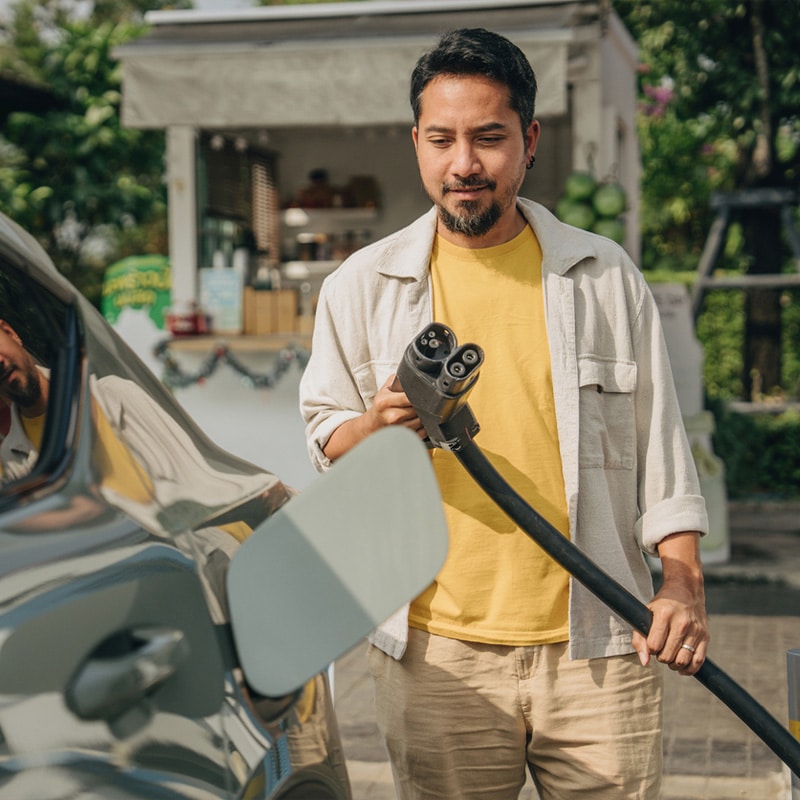 Man charging electric car at outdoor station, holding EV connector. Sustainable transportation concept.