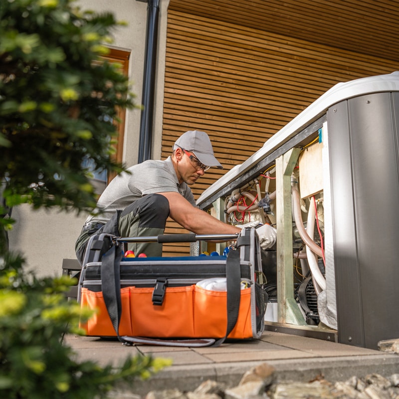 Technician repairing outdoor unit with tools on the ground, focused on HVAC maintenance.
