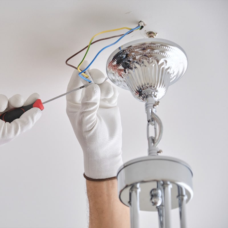 Electrician installing a ceiling light fixture with screwdriver and gloves.