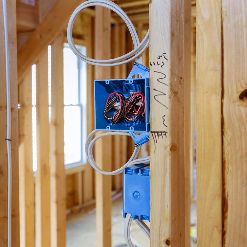 Electrical wiring in new construction with blue outlet box on wooden studs.