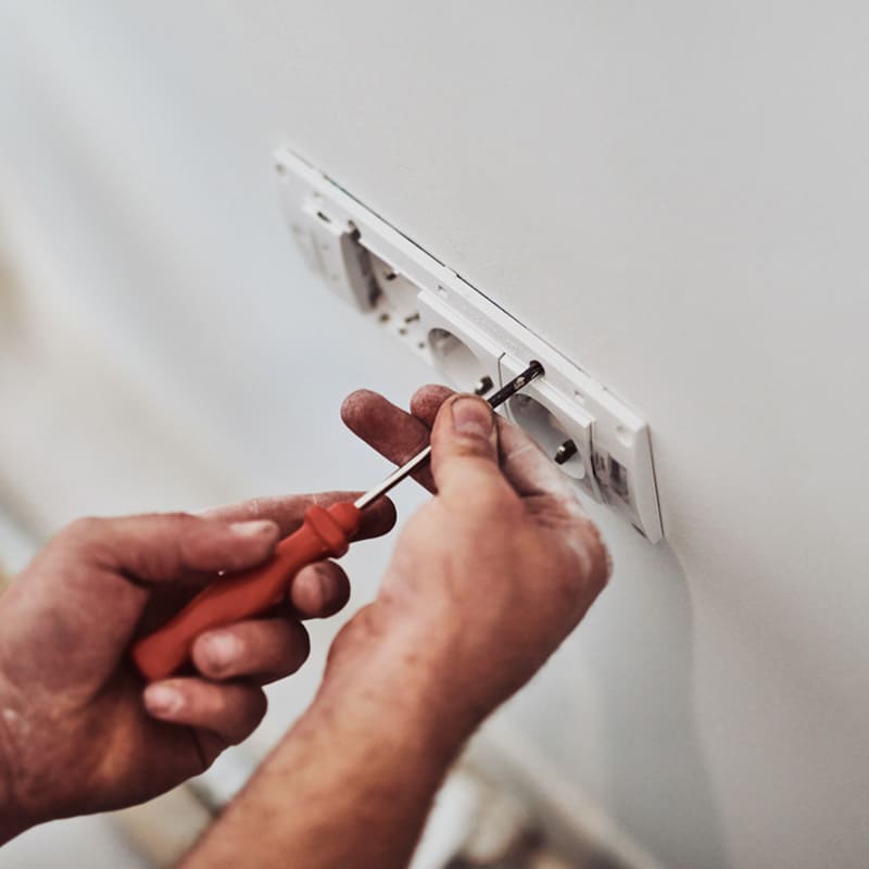 Person fixing wall socket with screwdriver; home electrical maintenance.