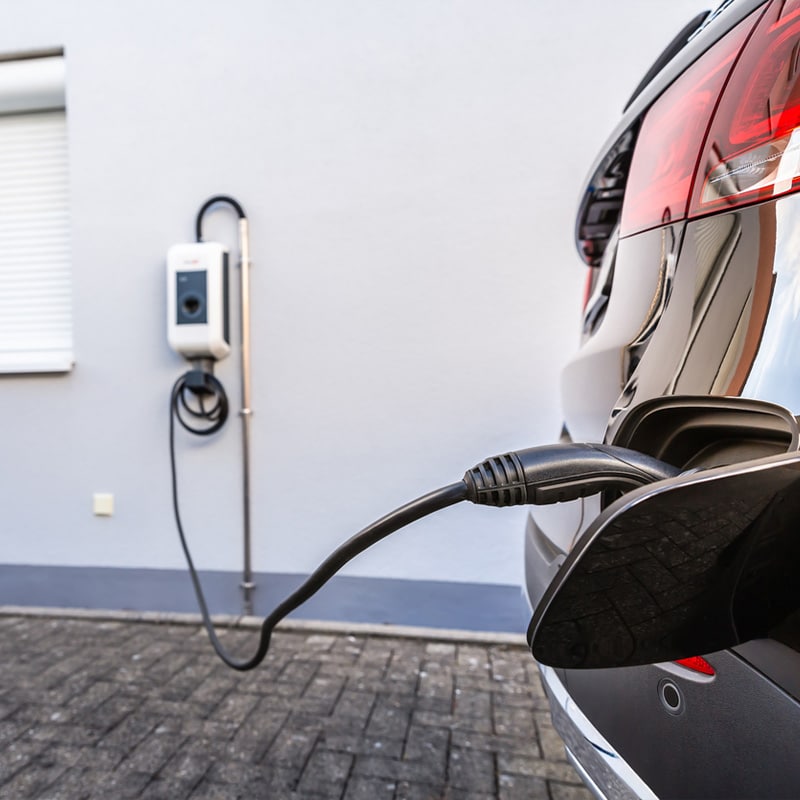 Electric vehicle charging at home with wall-mounted charger and plug.