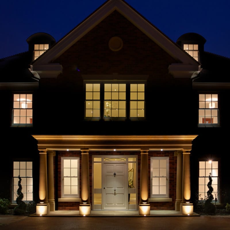 Elegant home exterior at night with warm lighting and classic architecture.